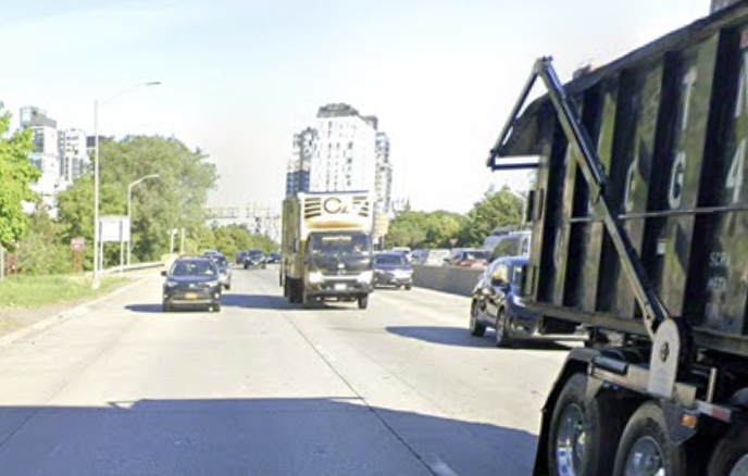 Sunken Major Deegan corridor with trucks and towers. The road sits below grade, so a lid decks upward over it.